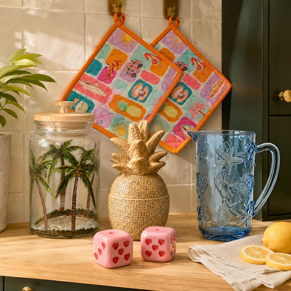 Keukenaccessoires met tropische voorraadpot, ananaspot, blauwe glazen kan, kleurrijke pannenlappen en roze peper- en zoutstel