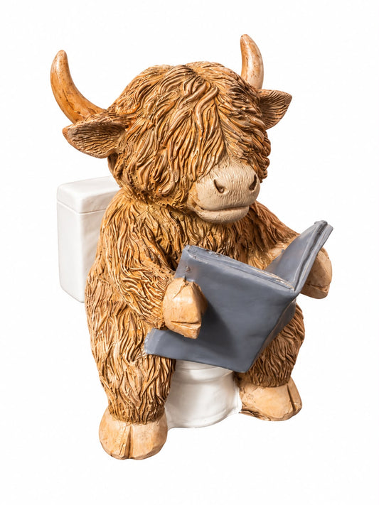 Grappig Schotse hooglander beeldje met bruine warrige vacht en horens, zittend op een wit toilet met een grijs boek, 11,5 cm hoog.