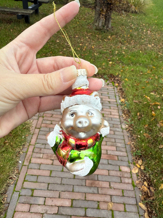 Glazen kerstornament in de vorm van een varkentje met groene jas, rode glitterdetails en rode muts – handgeschilderd – 10 cm hoog