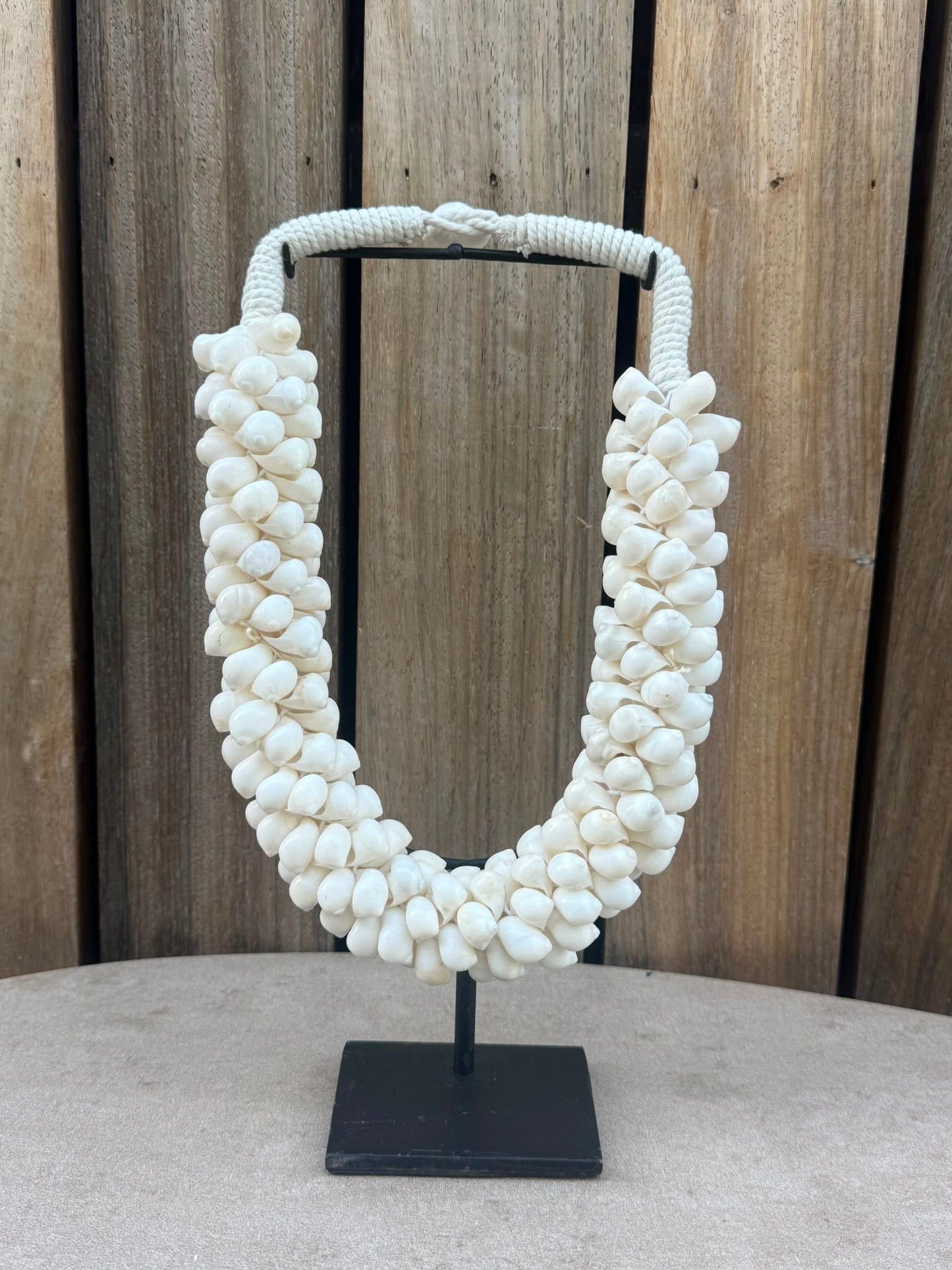 Handgemaakte schelpenketting van natuurlijke witte schelpen op een zwarte metalen standaard uit Indonesië.