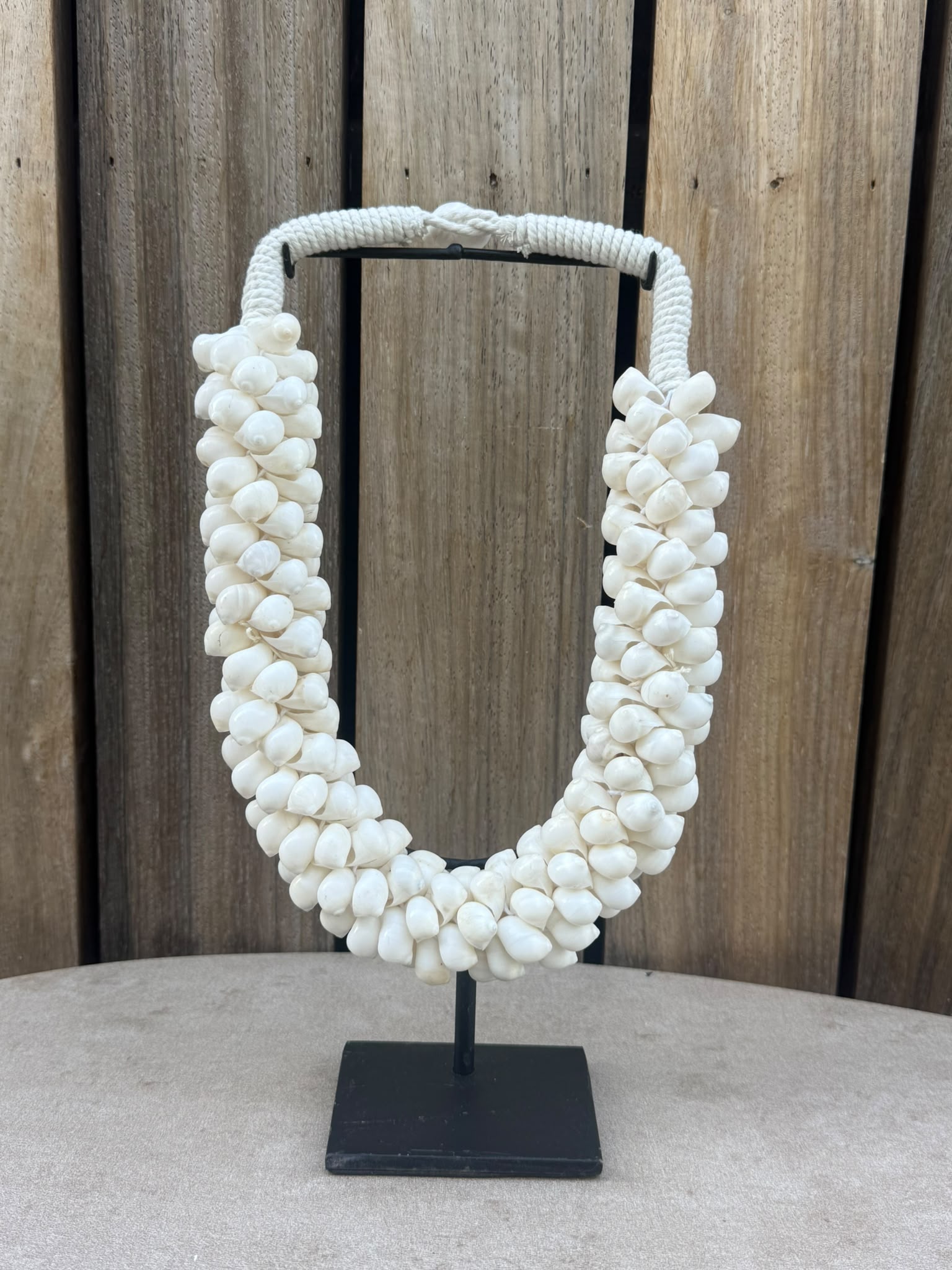 Handgemaakte schelpenketting van natuurlijke witte schelpen op een zwarte metalen standaard uit Indonesië.