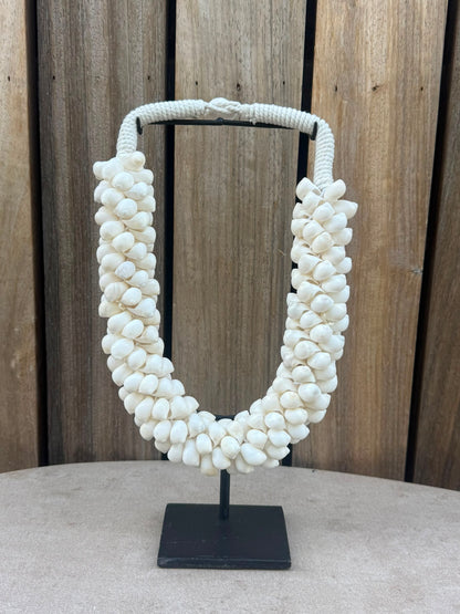 Handgemaakte schelpenketting van natuurlijke witte schelpen op een zwarte metalen standaard uit Indonesië.